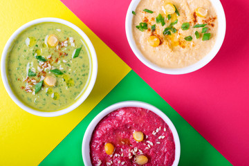 Colorful hummus in the white bowls against the geometric background. Classic, beetroot and spinach chickpea dips
