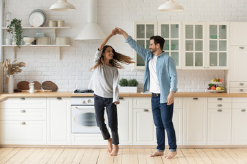 Happy loving couple having fun in kitchen, dancing together, celebrating relocation or anniversary,...
