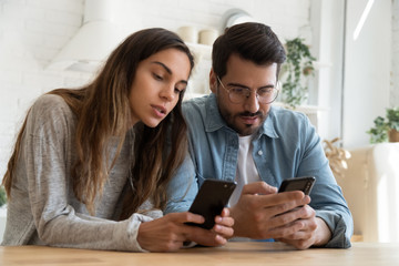 Young couple using smartphones, discussing news, mobile apps, looking at phone screens, serious man and woman holding cellphones, shopping online together, talking, checking message
