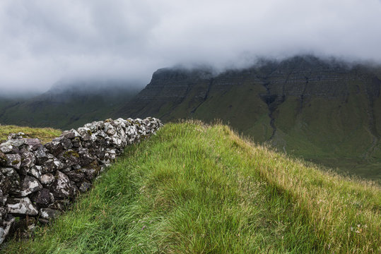 Fields and dry stone wall in front of mountain range, Faroe Islands