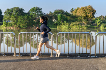 Portrait of young Asian woman running in the city on the street nearly waterfront. Running can significantly improve physical and mental health.