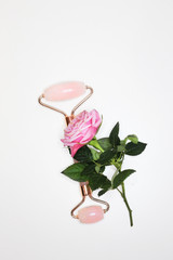 Face roller and pink rose on white background. Beauty tool anti aging. Face treatment device.