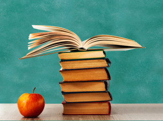 Back to school, pile of books and red apple with empty school board background, education concept.