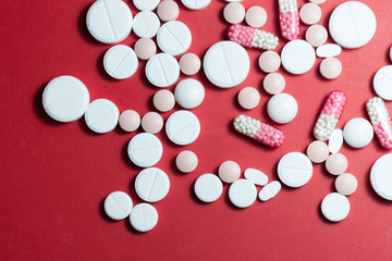 Heap of white pills, tablets, capsules on red background. Drug prescription for treatment medication health care concept wth copy space.