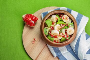 fruit salad in a wooden natural eco-friendly plate on a green background. fresh pomegranate, kiwi, banana