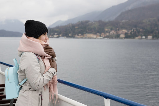 Passage Cruise Woman Tourist In Fjords Scandinavian Countries. Dressed In Hat, Scarf And Backpack. Looks Into Distance Mountains In Fog