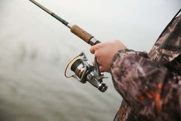 fisherman's hand holds fishing rod and spins fishing reel