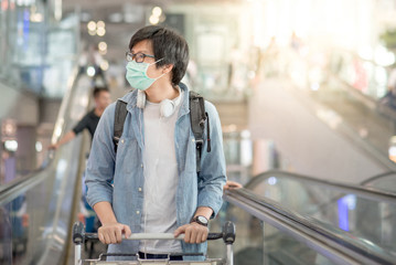 Asian man wear face mask walking with airport trolley and suitcase luggage in airport terminal....