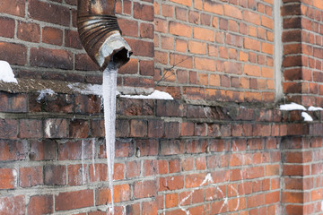 Rusty drainpipe with a large icicle on the background of a brick wall