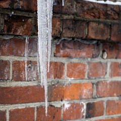A large icicle against a brick wall