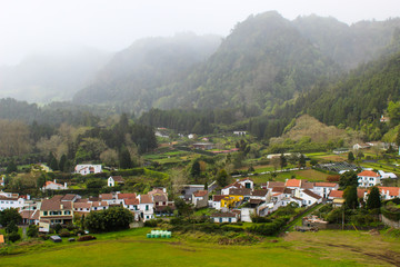 Fototapeta na wymiar Foggy mountain valley landscape with village surrounded by lush green rainforest