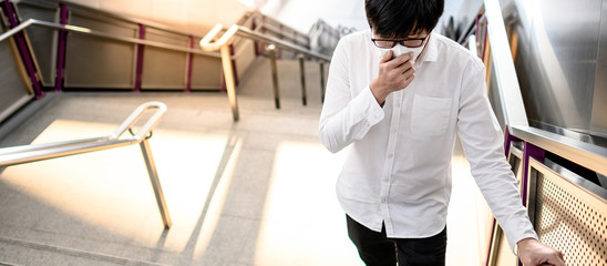 Asian man wearing face mask at skytrain station or urban train platform. Wuhan coronavirus...