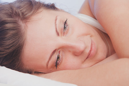Sleep and rest after hard and successful work. Close up portrait young beautiful woman falls asleep in bed with smile on her lips. Horizontal image.
