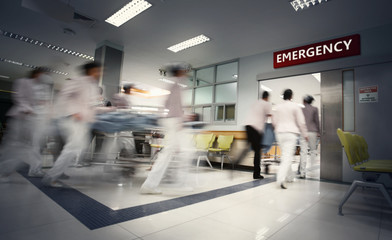 A motion blurred photograph of a patient on stretcher or gurney being pushed at speed through a...