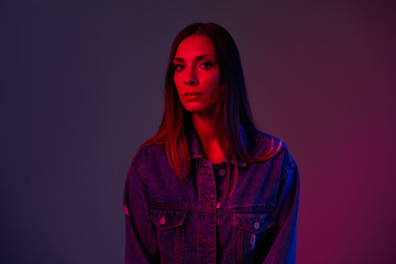 Close portrait of a caucasian young girl dressed. Denim jacket shot in studio with neon light.