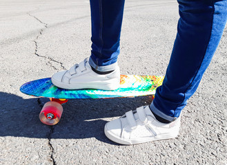 A young girl stands on a colorful penny board in the city, asphalt road. Healthy lifestyle, youth, teenager, child, sport, skateboard, active, entertainment. Side view of feet and board, close up