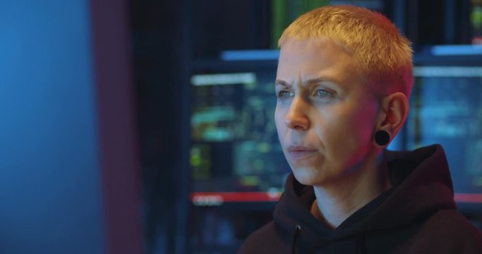 Close up of tired woman cyber police worker sitting in front of computer screen at night and working. Female hacker thinking hard while creating virus or antiviris. Difficult IT work concept.