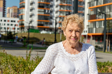 Relaxed elder woman sitting on a bench looking at camera and smiling. Happy old age concept