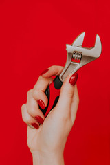female hand with a red manicure holds a tool. Adjustable wrench on a red background close-up. Concept: feminism, independence, autonomy