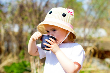 Child drinks water from a plastic cup  in the spring garden, holds a plastic cup in his hands