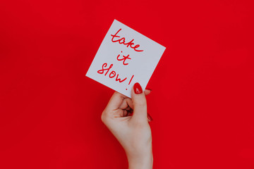 Note in a female hand with manicure, red nails. "Take it slow!" sign. Background red