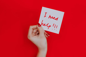 Note in a female hand with manicure, red nails. "I need help!!!" sign. Background red