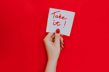 Note in a female hand with manicure, red nails. "Take it!" sign. Background red