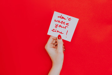 Note in a female hand with manicure, red nails. "don't waste your time!" sign. Background red