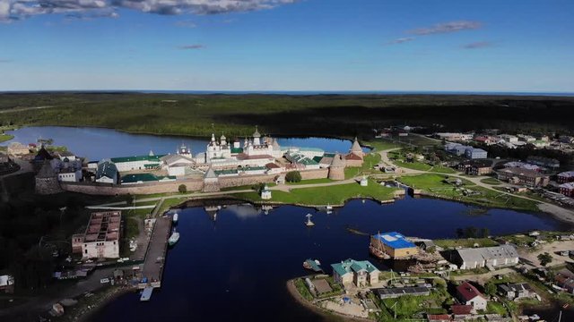 Smooth cinematic fly-by of the Solovetsky monastery from the seaside with a view over village and island on the sunny day. Solovetsky monastery is an old (1420) ROC monastery.