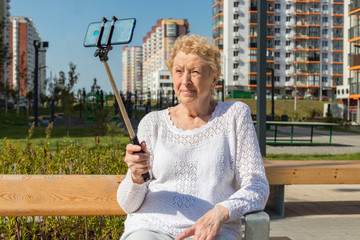 Relaxed elder woman sitting on a bench and makes selfie with smartphone. Happy old age concept