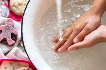 Fototapeta premium Child’s hands under white bowl with water upon water stream, colorful soaps on a white material, cleanliness and hygiene concept 