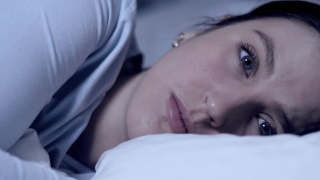 Girl can not fall asleep. Insomnia concept. Young attractive caucasian girl lies in alone in bed blinking and looking at camera. Close-up
