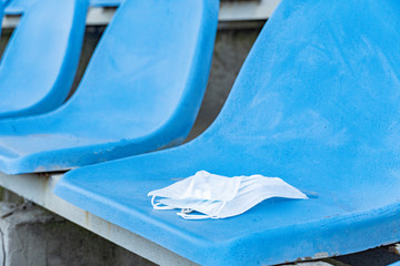 A medical mask is lying on a stadium chair. Empty stands.Protection of the crown from viruses and bacteria ceases. Cancellation of sporting events. Rows of chairs in an open stadium.