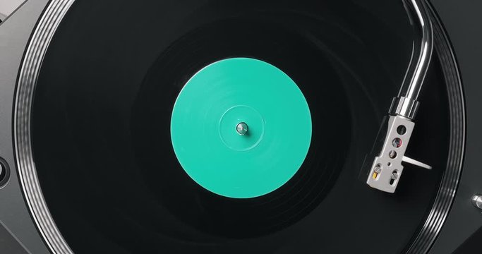 Black vinyl record on DJ player. Black vinyl background green label in center. Rotating plate close-up on turntable. Needle stylus. Macro Top view. Popular styles of disco from 90s, 70s, 80s. Party