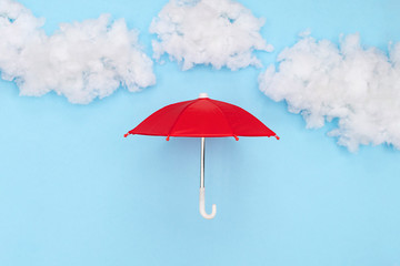 Red umbrella place under a puffy cotton stuffing on a sky blue background
