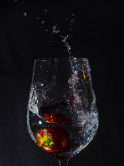 Cup with water falling from a strawberry, with splash in drops