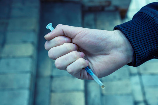 Addict holding a syringe in his hand on a dark background. Tinted photo.