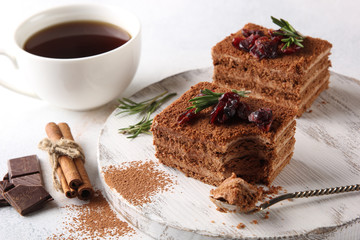 Dessert. Chocolate biscuit cake with cream, cinnamon and berries. Sweet pie with cocoa and chocolate on a white wooden board. Cup of coffee and rosemary on a light background. Copy space