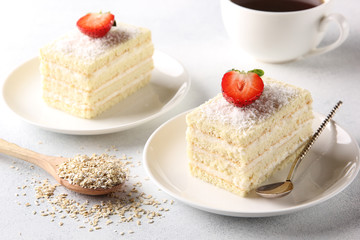 Dessert. White biscuit cake with cream and coconut shavings on white plate with spoon. A ?up of coffee and strawberry on a light background. Background image, copy space