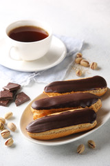 Dessert. Eclairs with chocolate glaze with a cup of coffee. Cake with cream. Chocolate, pistachios on a light background. Background image, copy space