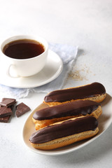 Dessert. Eclairs with chocolate glaze with a cup of coffee. Cake with cream. Chocolate on a light background. Background image, copy space