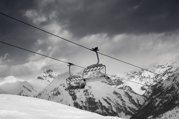 Chair lift, snowy ski slope, high winter mountains and dark cloudy sky