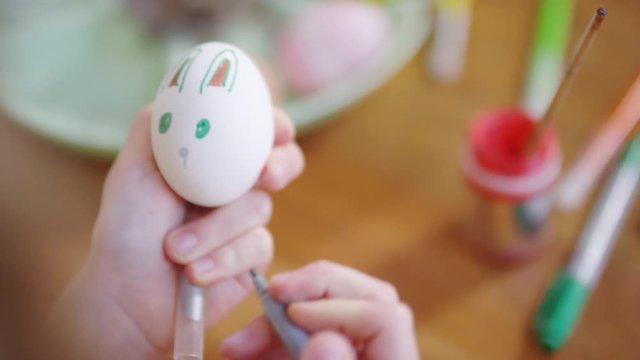 Close up shot of hands of unrecognizable child using felt tip pen and drawing bunny face on white Easter egg