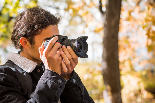 Side view of young man photographer in autumn forest taking photos of beautiful fall weather