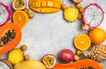 Set of exotic tropical fruits on light gray background - papaya, mango, pineapple, dragon fruit, orange, coconut, passion fruit, longan. Top view