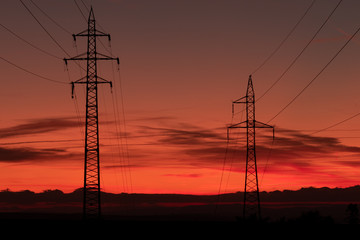 Silhouette of high voltage lines and transmission towers thru the Moravian field at sunrise