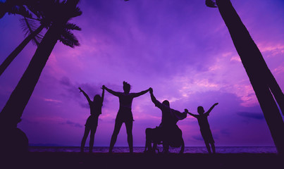 Disabled man in a wheelchair with his family on the beach. Silhouettes at sunset