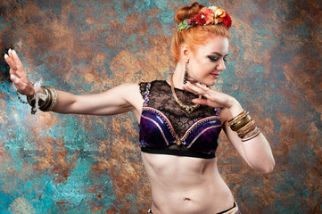 beautiful woman in tradition tribal costume with vest and red wreath with flowers stay in pose in front of teal and orange background in studio