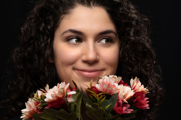 Naklejka premium Attractive smiling cheerful brunette woman holding bouquet of rosy and red flowers. Happy curly female model enjoying the moment. Black background...