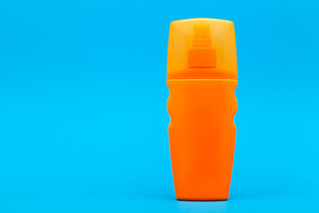 orange unlable bottle of sunscreen on a blue background with copy space.